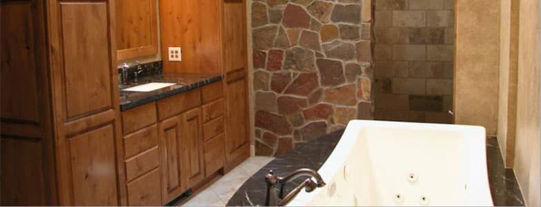 Master bathroom with alder cabinets, a fieldstone wall and a jetted tub